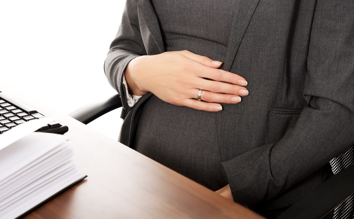 A pregnant woman is sitting at a desk rubbing her belly as she contemplates contacting Chicago discrimination lawyers to know her workplace rights.