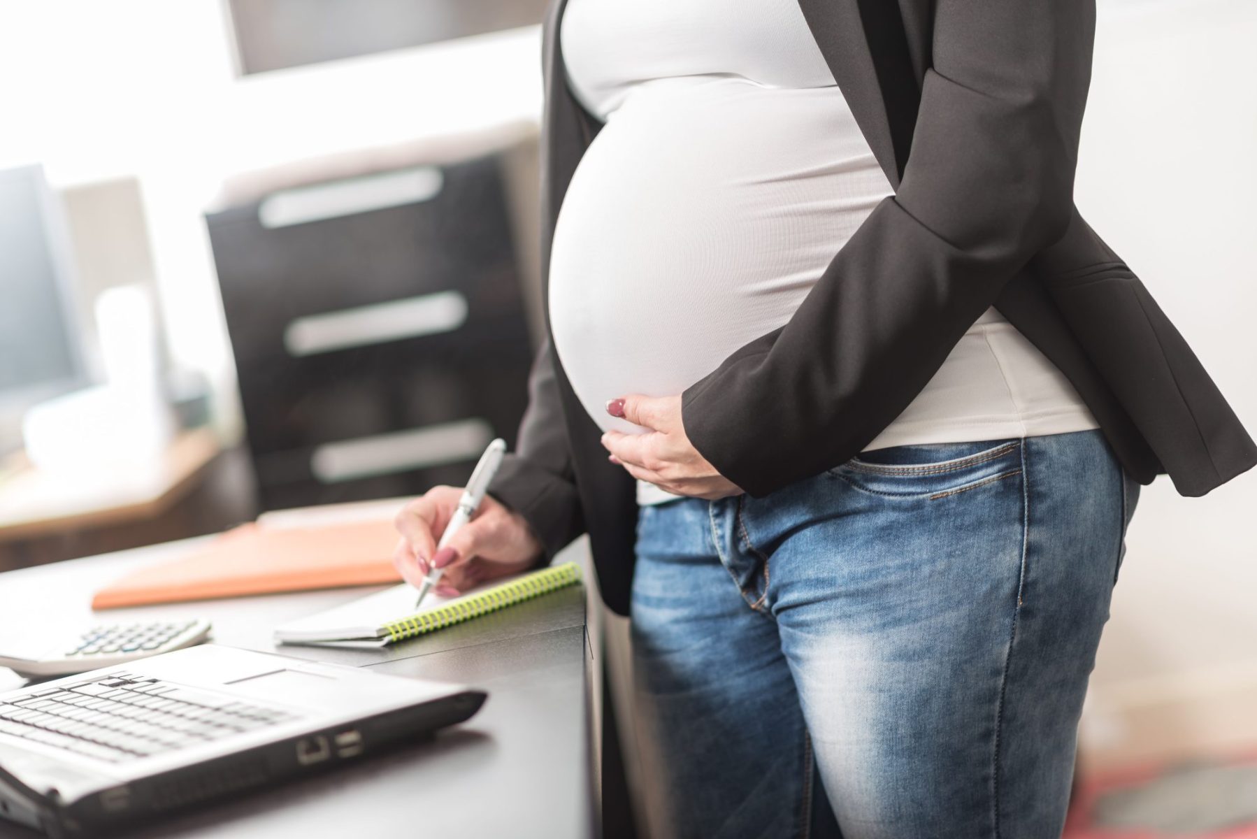 Pregnant woman standing at desk at work to represent Pregnancy Discrimination Attorney Near Chicago when terminated wrongly.
